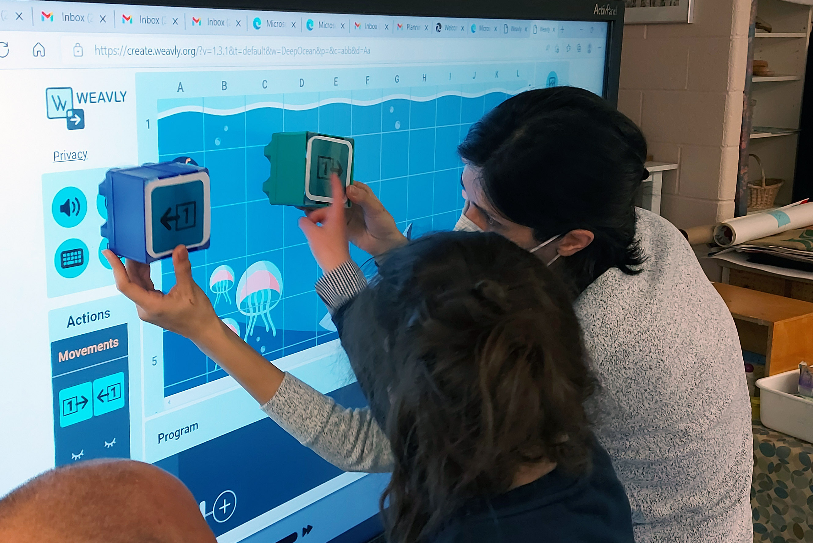 Facilitator and a student are using both physical direction blocks and the Weavly coding environment to explore different coding challenges. Facilitator and the student are working together using physical and digital tools to explore different ideas.